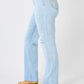 Woman wearing high waist distressed straight jeans by Judy Blue, side view with light blue denim and tan boots.