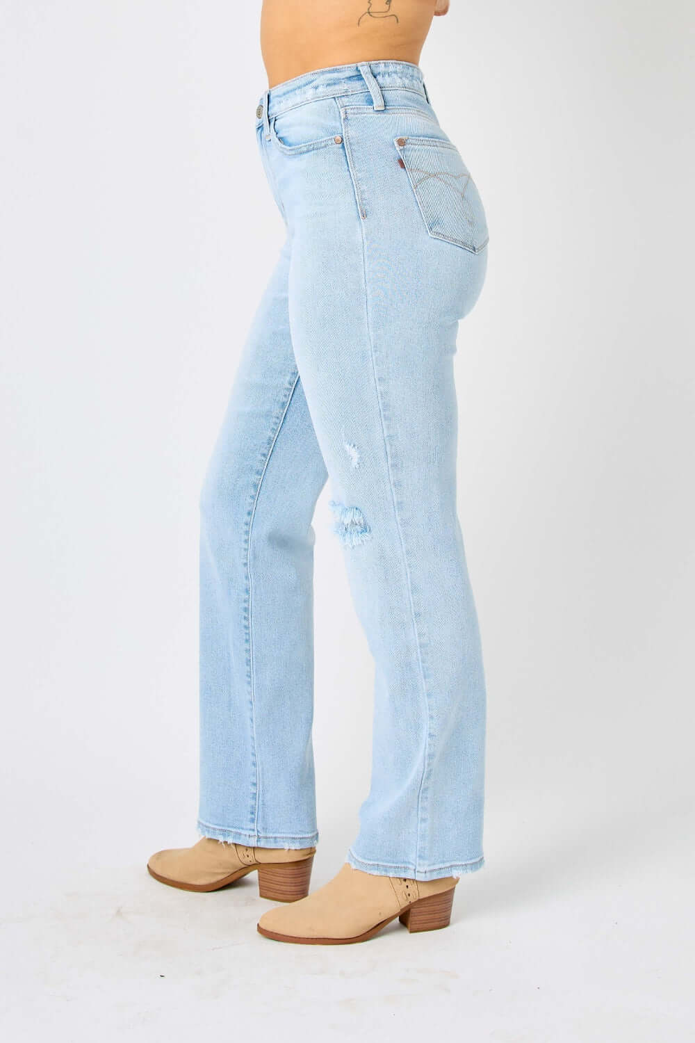 Woman wearing high waist distressed straight jeans by Judy Blue, side view with light blue denim and tan boots.