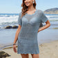 Model wearing Bella Road Swim Openwork Round Neck Short Sleeve Cover-Up on a beach with waves in the background.