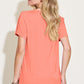 Woman wearing a Bamboo V-Neck High-Low T-Shirt in coral, showing back view with slightly stretchy material suitable for casual wear.