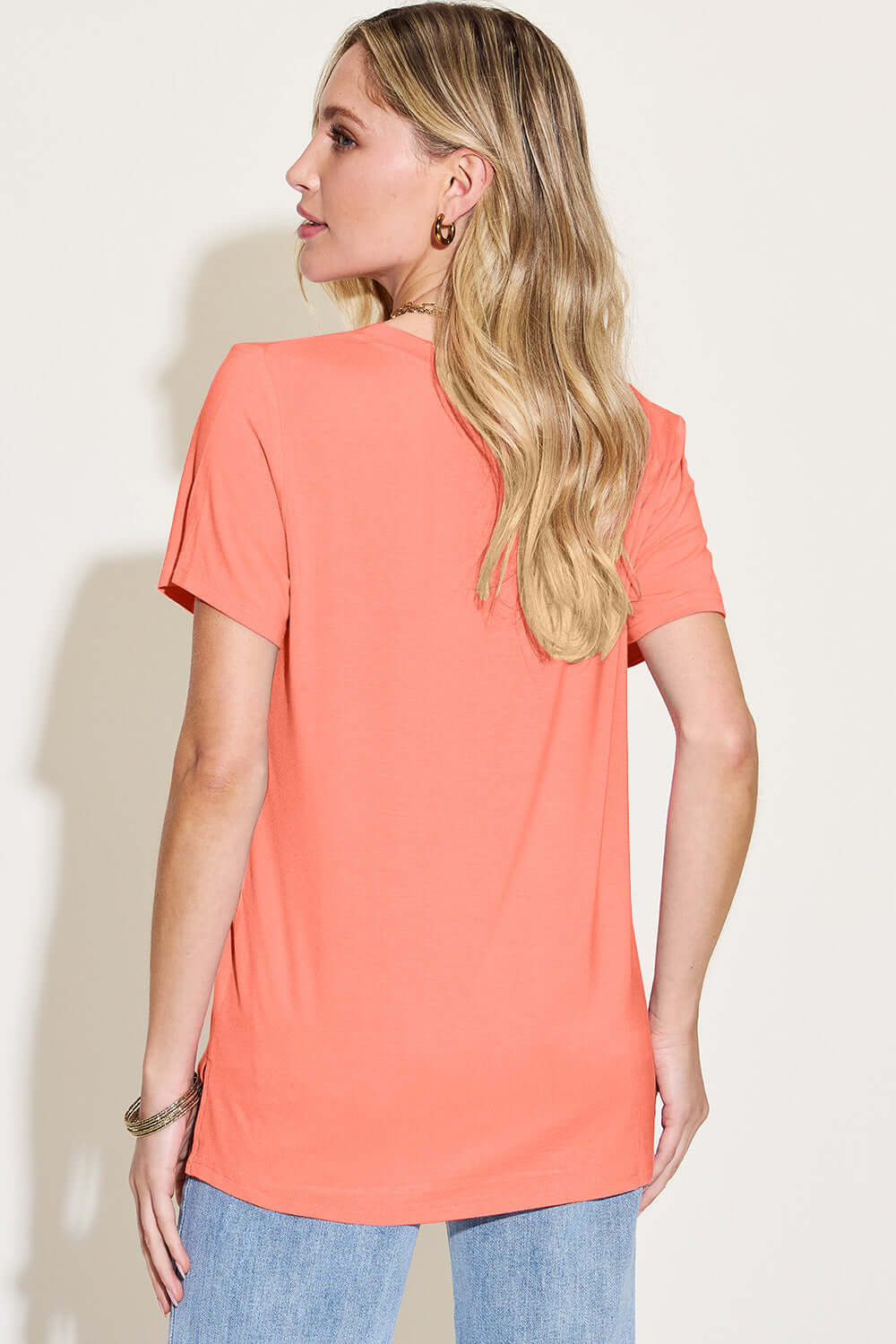 Woman wearing a Bamboo V-Neck High-Low T-Shirt in coral, showing back view with slightly stretchy material suitable for casual wear.