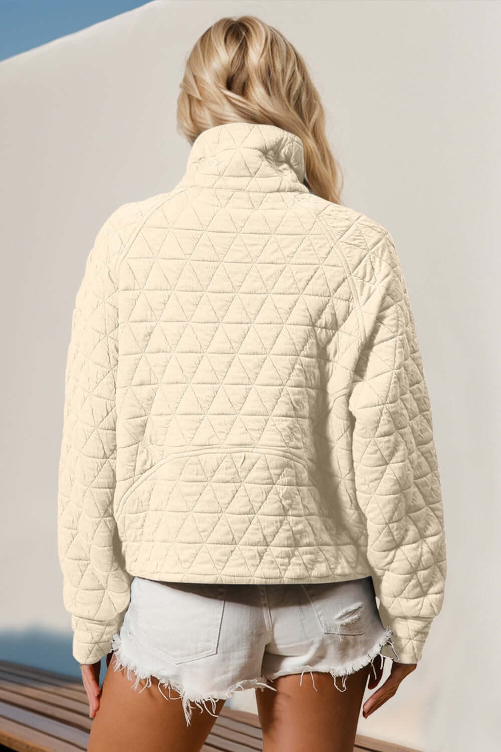 Woman wearing cream quilted sweatshirt with half zip and pocket, showcasing cozy and stylish design against a neutral background.