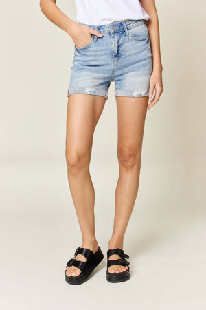 Woman wearing high-waist rolled denim shorts by Judy Blue Jeans paired with black sandals and a white t-shirt.