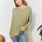 Woman wearing an oversized super soft rib layering top with sharkbite hem and round neck in light green, paired with jeans.