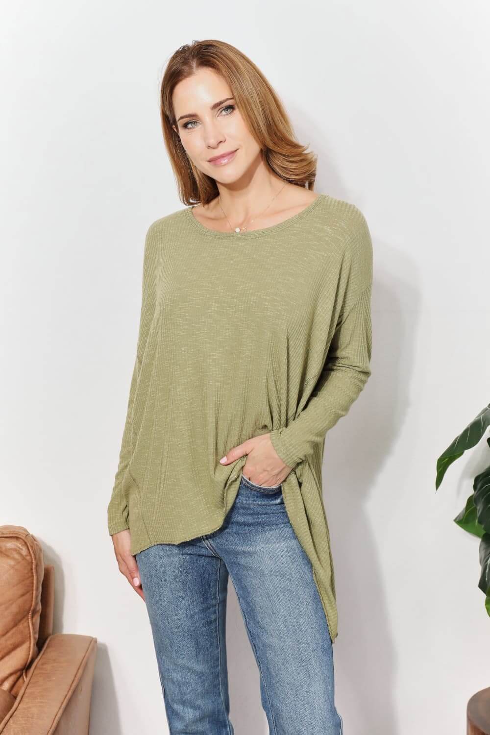 Woman wearing an oversized super soft rib layering top with sharkbite hem and round neck in light green, paired with jeans.