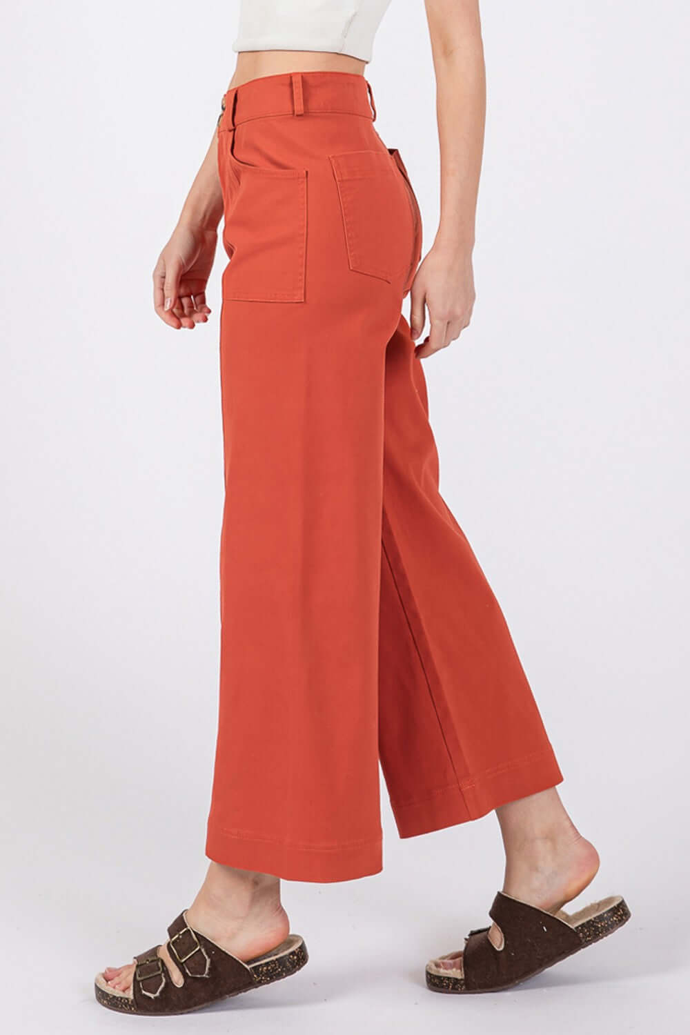 Woman wearing wide-leg cropped pants in rust color with front and back pockets, showcasing a comfortable and stylish design with sandals.