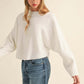 Woman wearing Bella Road Mable Round Neck Dolman Sleeve Cropped Sweater with blue jeans and black baseball cap