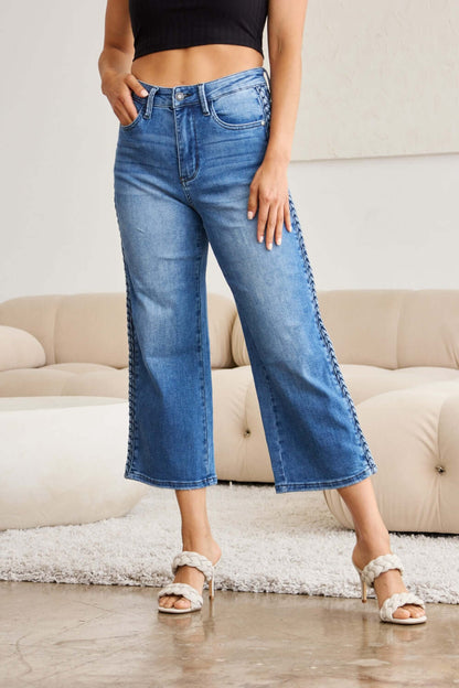 Woman wearing Judy Blue wide leg jeans with braid side detail while posing in a modern living room