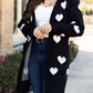 Woman wearing Bella Road Heart Open Front Long Sleeve Cardigan with white heart patterns, paired with a white top and jeans.