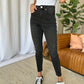 Woman wearing RFM Full Size High Rise Tummy Control Skinny Jeans with a white top and black sneakers in a stylish living room.