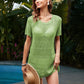 Model wearing Bella Road Swim Openwork Round Neck Short Sleeve Cover-Up in green by the pool surrounded by tropical plants.