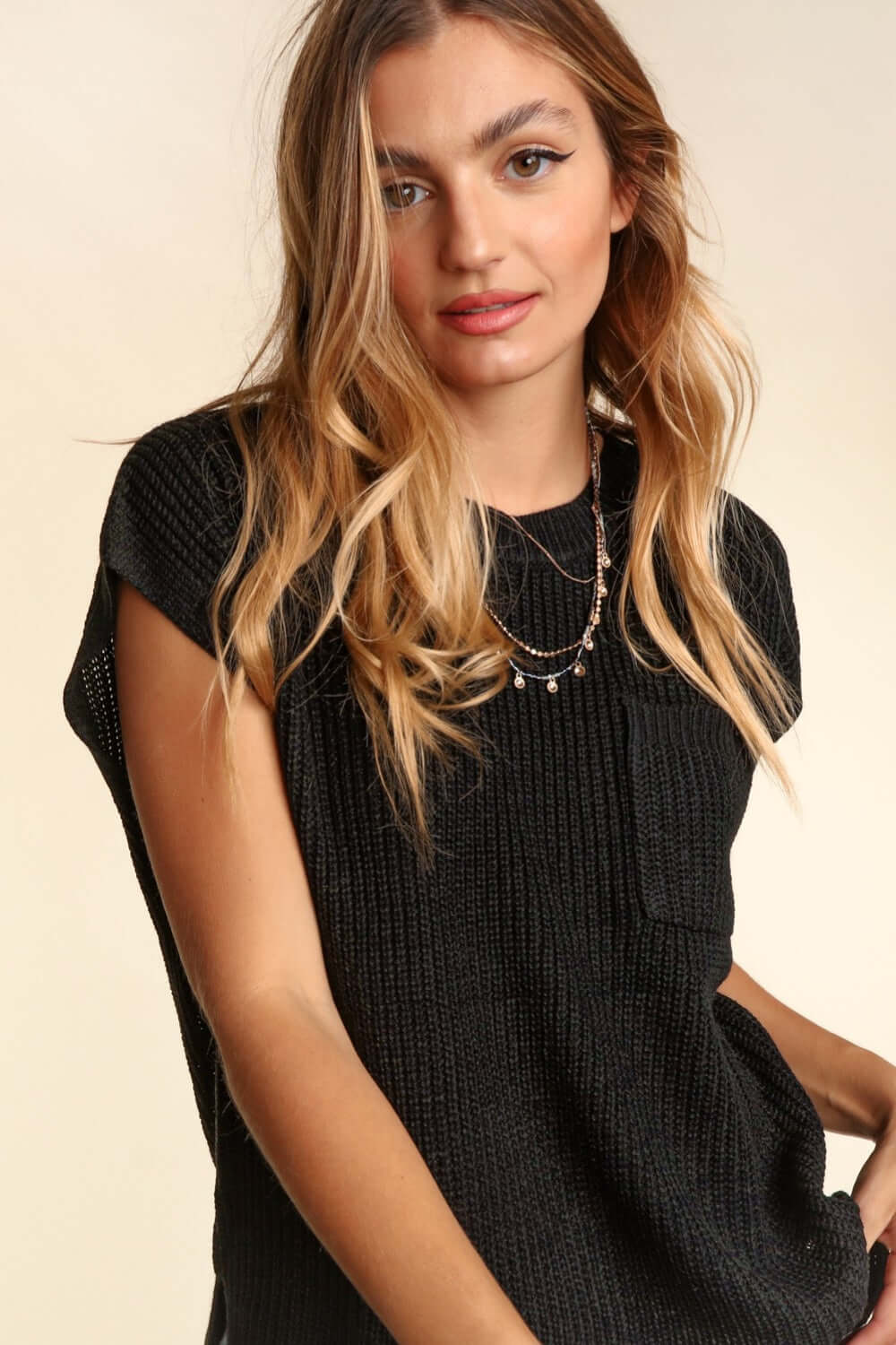 Woman wearing Pocketed Round Neck Cap Sleeve Knit Top in black, styled with a necklace, showcasing a casual and elegant look.