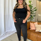 Woman wearing RFM Full Size High Rise Tummy Control Skinny Jeans with a black top, standing confidently in a cozy, modern room.