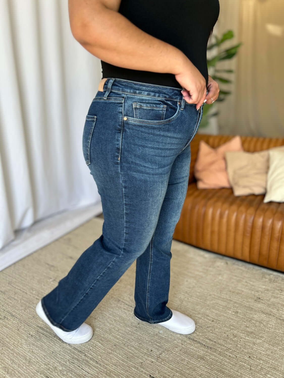 Woman wearing RFM Full Size High Rise Straight Tummy Control Jeans in a living room setting