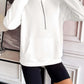 Woman wearing Ivy Lane Half Zip Raglan Sleeve Sweatshirt in white with front pocket and black shorts standing indoors.