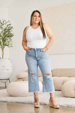 Woman wearing Tummy Control High Waist Raw Hem Distressed Jeans, full-size, standing in a stylish living room.