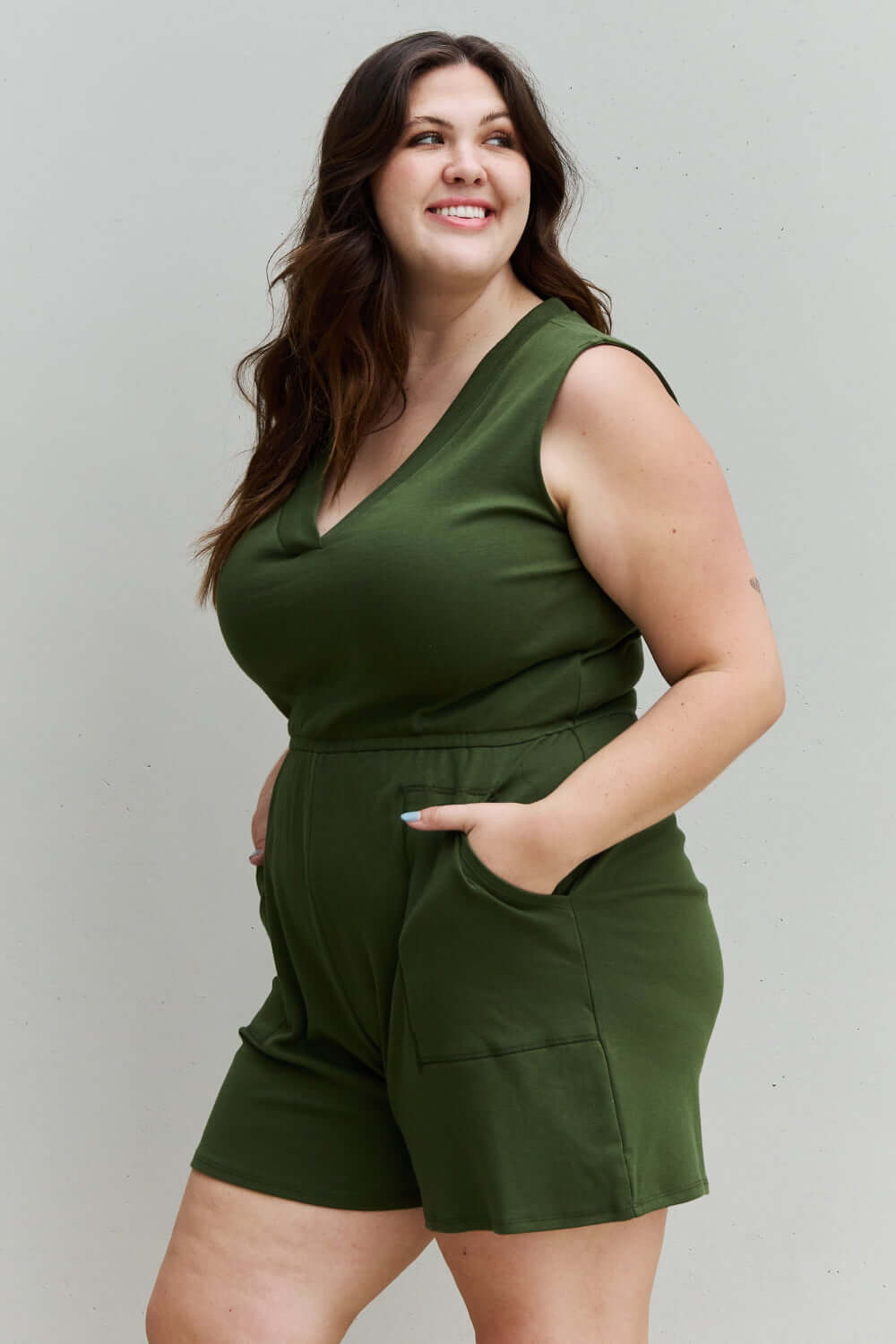 Plus-size model wearing Forever Yours V-Neck Sleeveless Romper in Army Green with hands in pockets