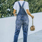 Woman wearing pocketed distressed denim overalls with acid wash outdoors, paired with a white t-shirt and beige high-heeled sandals.