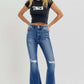 Woman wearing trendy high rise distressed flare jeans with raw hem, styled with a black crop top, showcasing modern fashion.