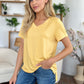 Woman wearing a yellow Bamboo V-Neck High-Low T-Shirt with blue jeans standing in a cozy living room