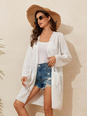 Woman wearing a white lace detail open front long sleeve cover-up over a white tank top, paired with denim shorts and a straw hat.