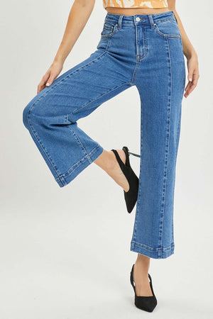 Model wearing Risen Jeans high-rise wide-leg jeans for petite in blue denim, paired with black heels.