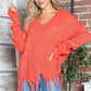 Woman wearing Bella Road frayed hem dropped shoulder sweater in vibrant orange with casual jeans, posing in a stylish room.