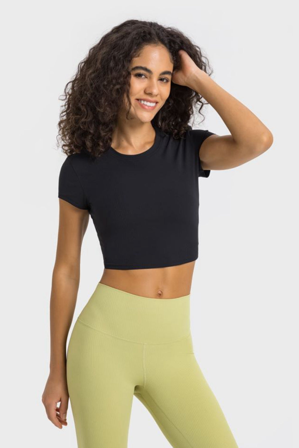 Young woman in black cropped sports t-shirt and green leggings, perfect for yoga or fitness activities.