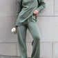 Stylish woman in green turtleneck side slit sweater and matching pants, holding coffee cup, showcasing cozy, relaxed fashion style.