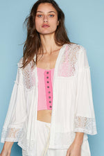 Woman wearing a white open front lace detail cardigan with 3/4 length bell sleeves over a pink top