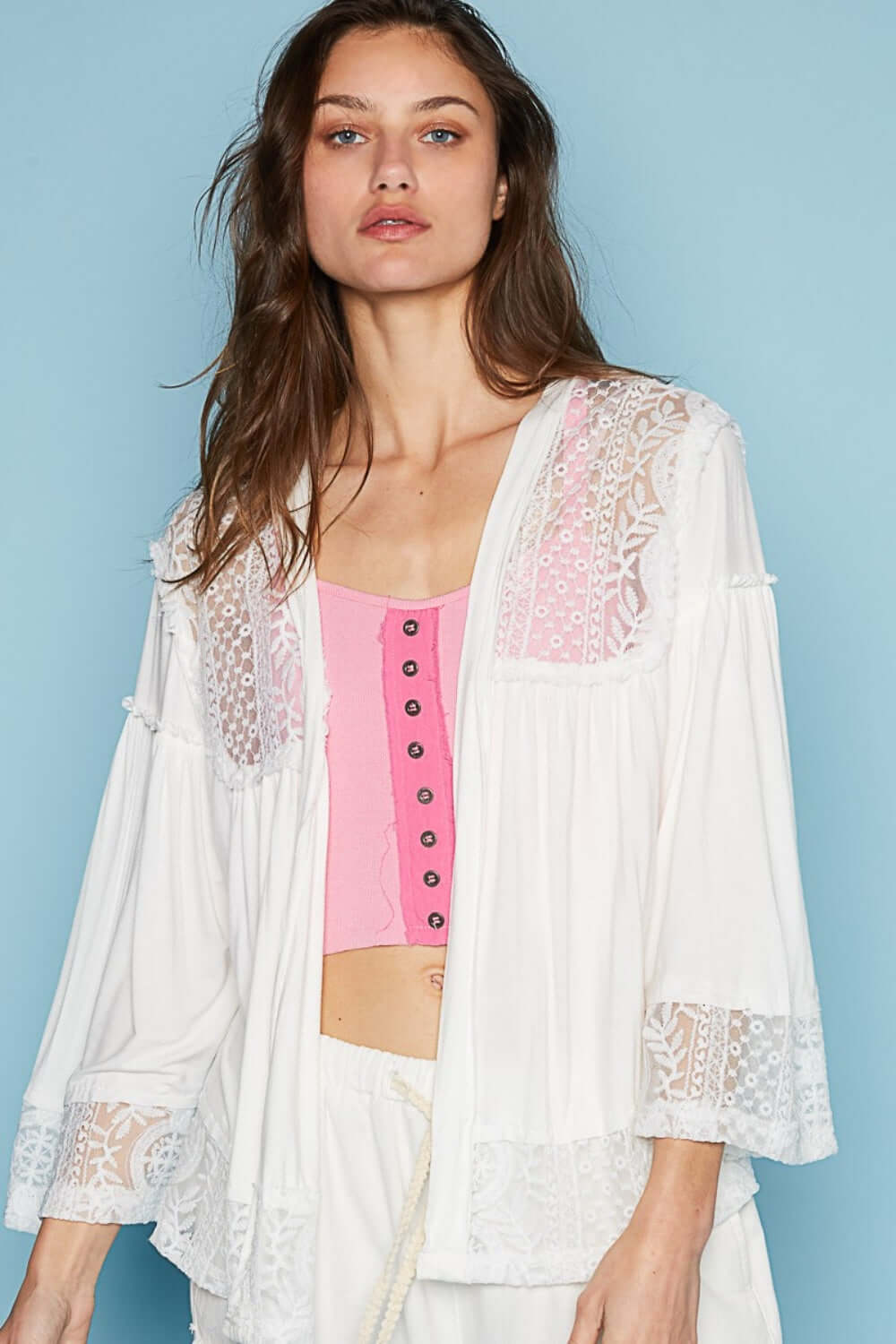 Woman wearing a white open front lace detail cardigan with 3/4 length bell sleeves over a pink top