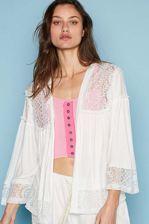 Woman wearing a white open front lace detail cardigan with 3/4 length bell sleeves over a pink top