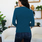 Woman wearing a FAM-FAM Ruched Mock Neck Long Sleeve T-Shirt in French Blue, standing in a stylish room with plants and decor.