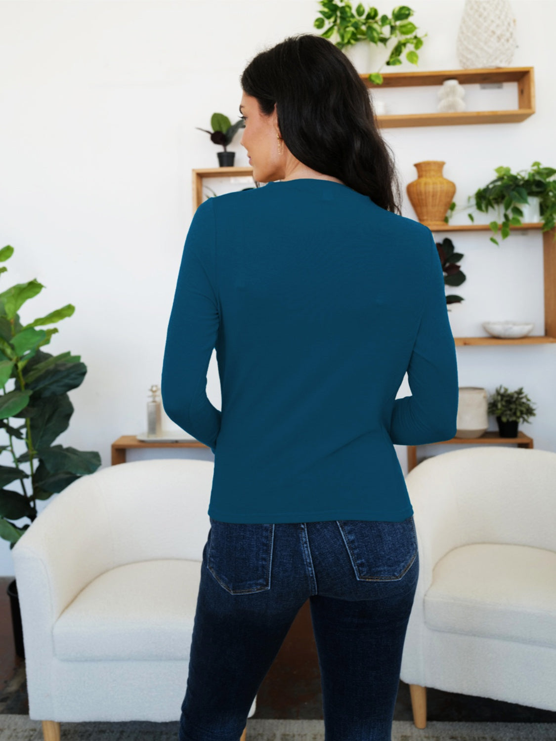 Woman wearing a FAM-FAM Ruched Mock Neck Long Sleeve T-Shirt in French Blue, standing in a stylish room with plants and decor.