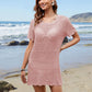 Woman in a pink openwork cover-up smiles on the beach, showcasing summer style and comfort by the waves.