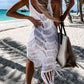 Woman in a white fringe cover-up walking on the beach, showcasing bohemian style and summer vibes.