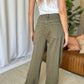 Woman wearing high-rise garment dye wide leg jeans in green, showcasing back pockets and relaxed fit in a stylish indoor setting.