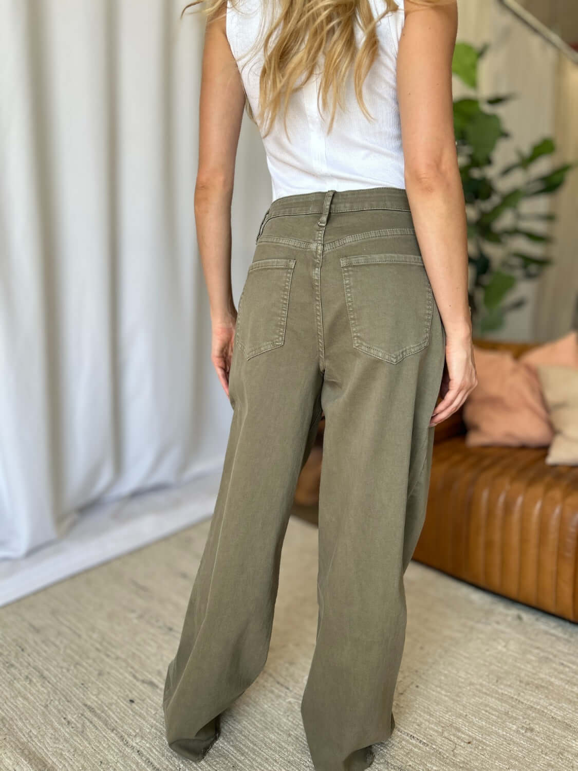 Woman wearing high-rise garment dye wide leg jeans in green, showcasing back pockets and relaxed fit in a stylish indoor setting.