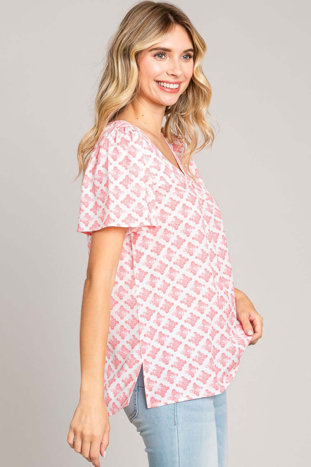 Woman wearing Slit Printed V-Neck Flutter Sleeve Blouse in pink and white, showcasing delicate flutter sleeves and subtle slit detail.