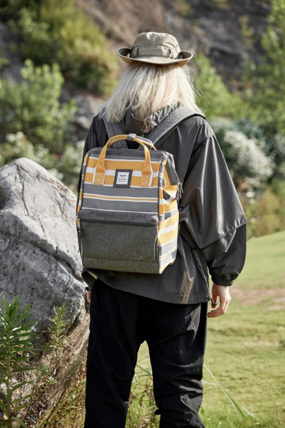 Fashionable striped waterproof nylon backpack with side pockets showcased outdoors by a hiker in nature.