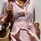 Woman wearing Bella Road Tied Button Up Three-Quarter Sleeve Dress with striped pattern, accessorized with jewelry and a woven handbag