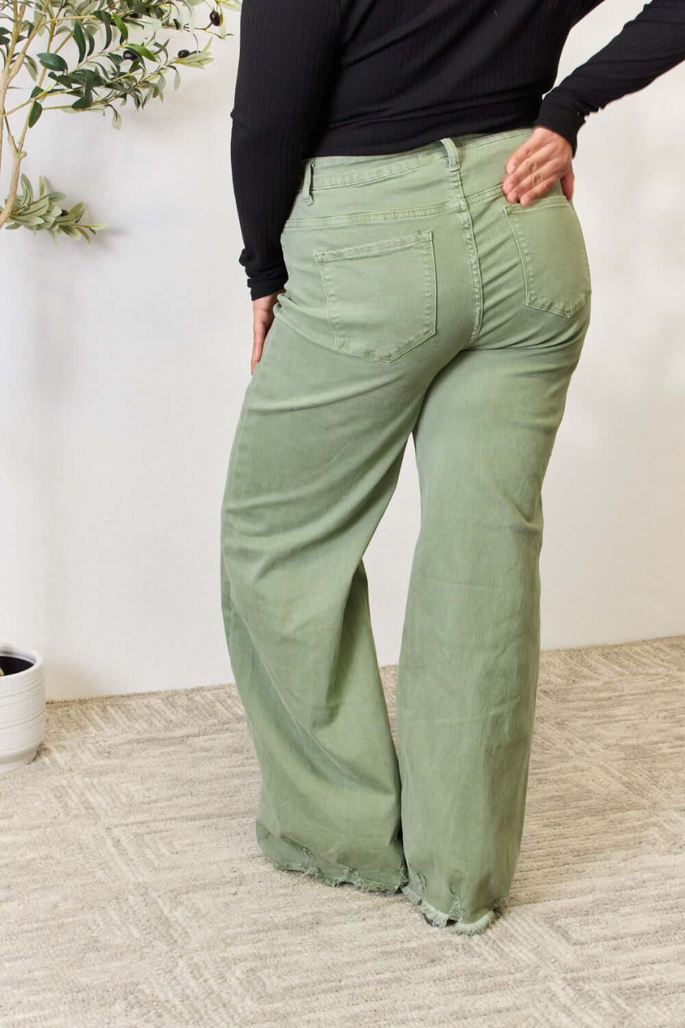 Woman modeling Risen Raw Hem Wide-Leg Jeans in sage green, showcasing high-waisted fit and trendy wide-leg design with back pocket details.