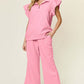 Woman wearing pink texture ruffle short sleeve top and drawstring wide leg pants set with pockets.