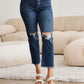 Woman wearing RFM Jeans Tummy Control Distressed High Waist Raw Hem Jeans standing in modern living room.