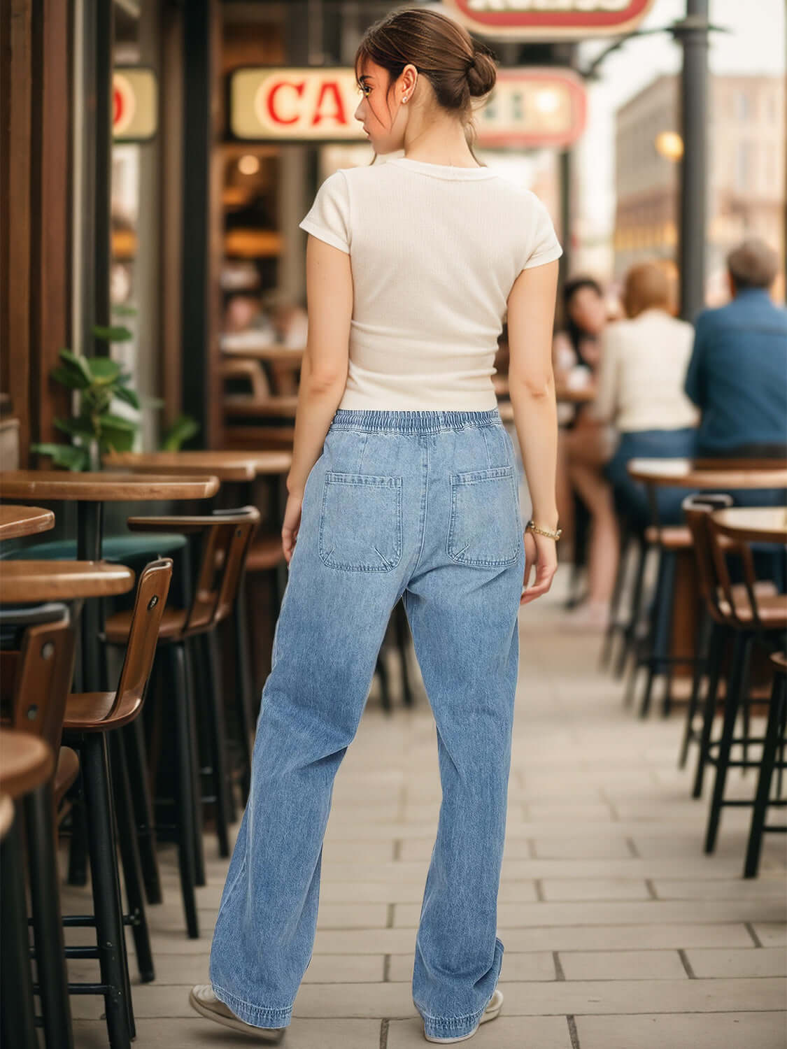 Woman wearing drawstring straight jeans with pockets, standing in outdoor cafe setting.