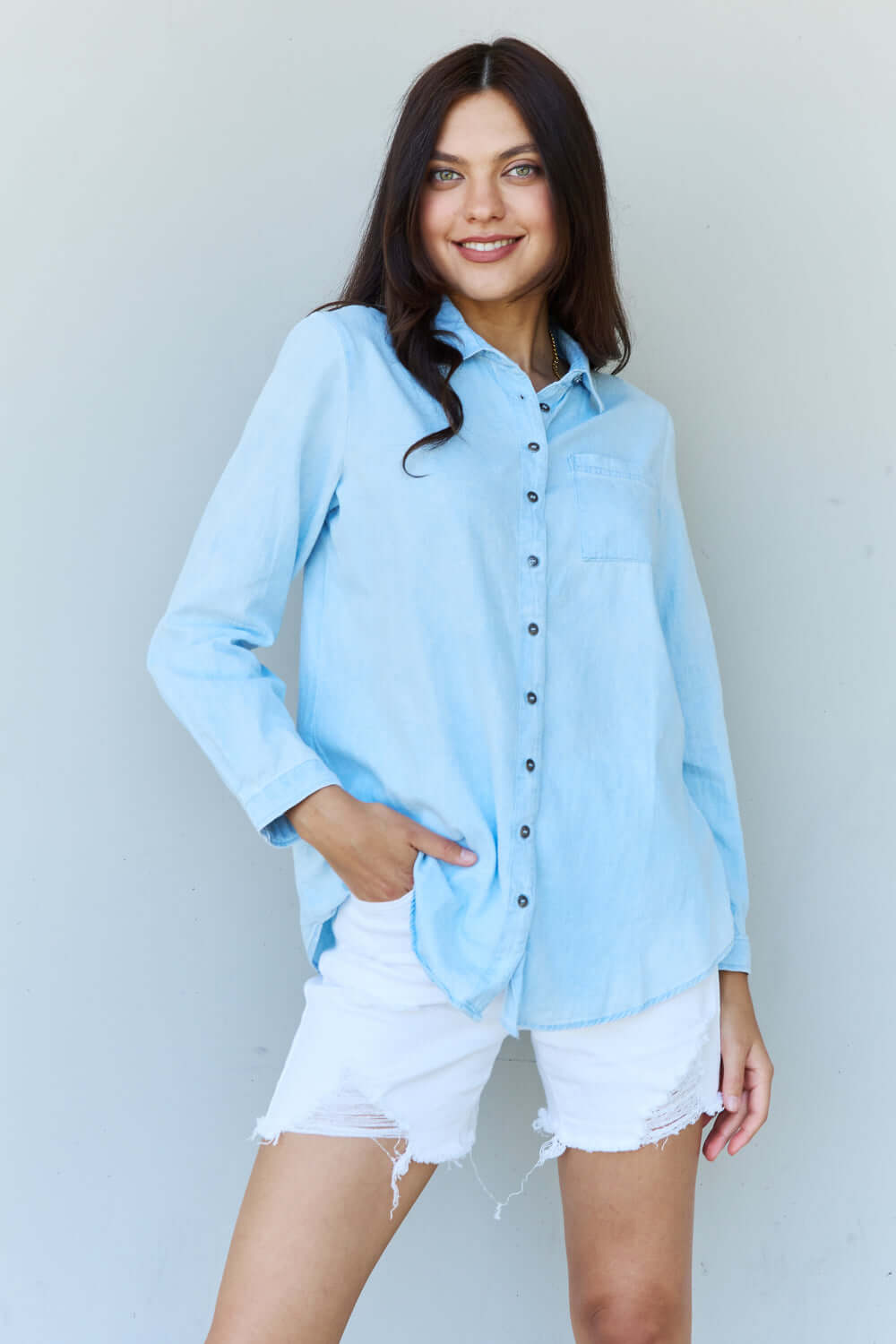 Woman wearing Blue Jean Baby Denim Button Down Shirt Top in Light Blue paired with white shorts.