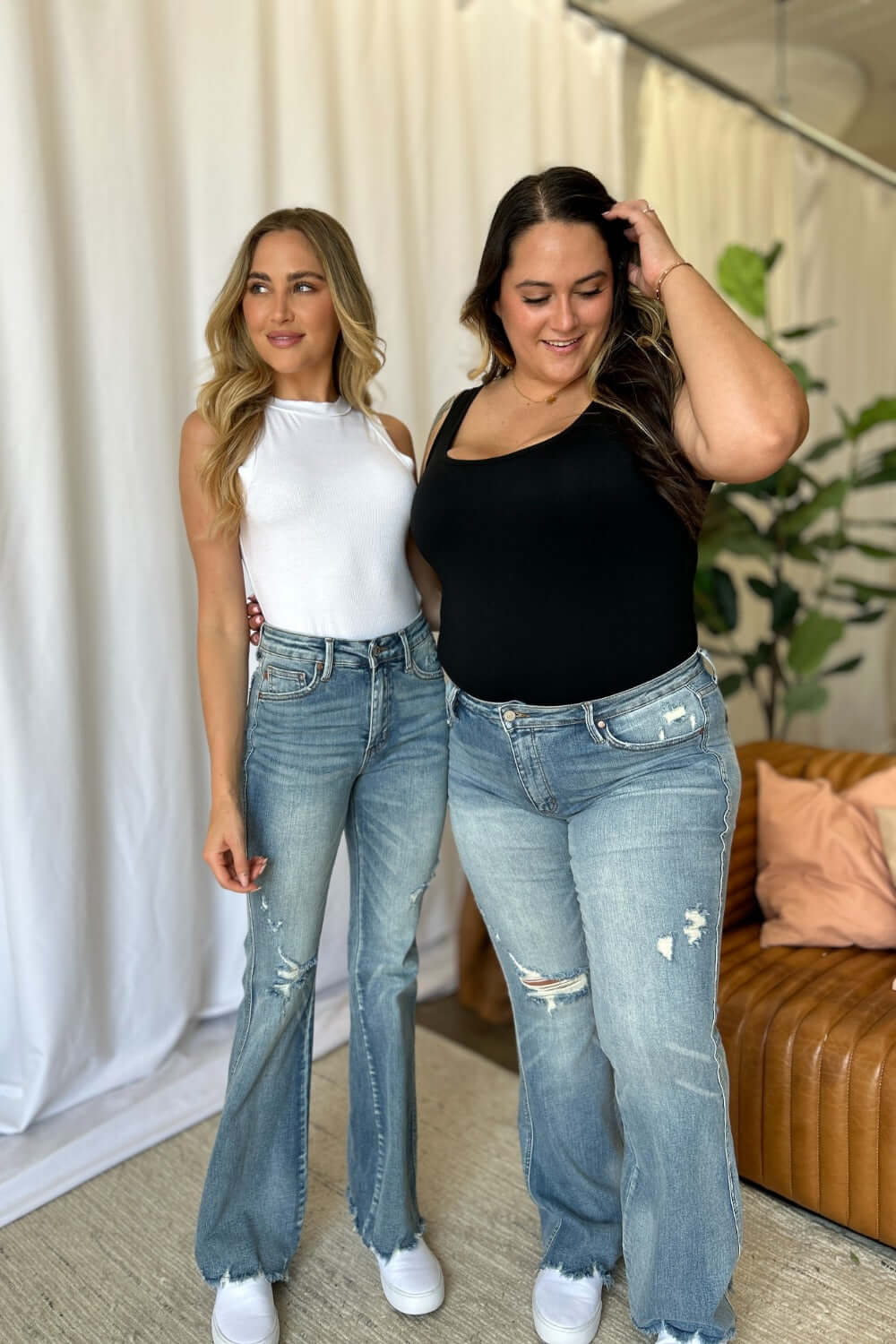 Two women wearing Judy Blue medium rise tummy control destroy flare jeans in a stylish indoor setting.