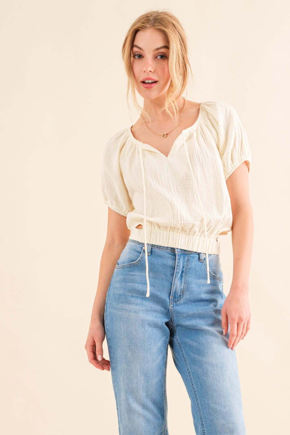 Woman wearing Back Waist Tie Cropped Blouse with short sleeves, paired with blue high-waisted jeans.