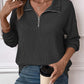 Woman wearing a striped half zip long sleeve t-shirt in dark gray with blue jeans, holding a coffee cup, and accessorized with gold jewelry.