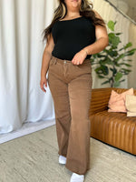 Woman wearing RFM Full Size High Rise Garment Dye Wide Leg Jeans in a stylish, relaxed fit, paired with a black top in a chic, minimalist setting.